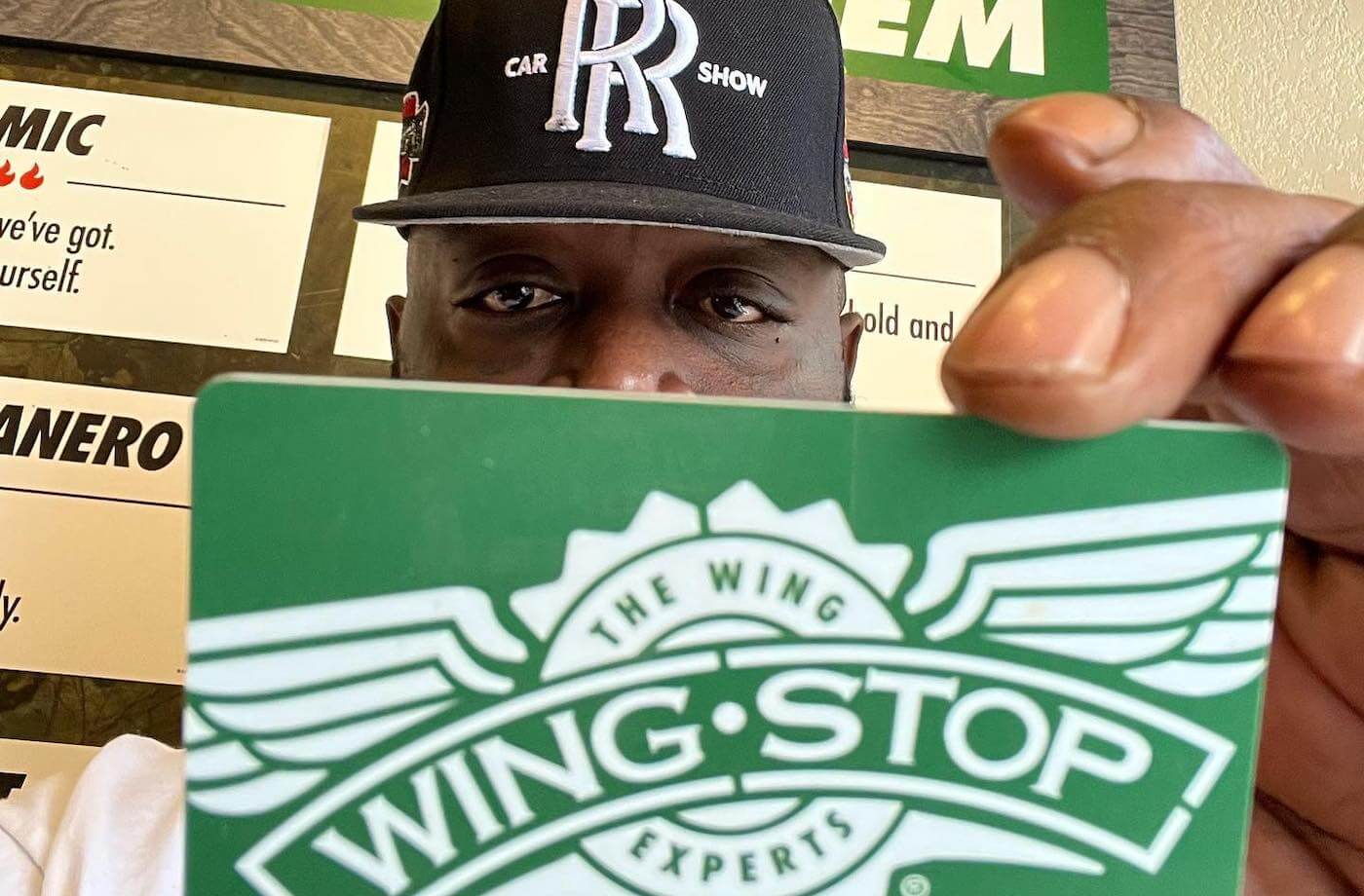 rick ross holds a wingstop gift card up to the camera
